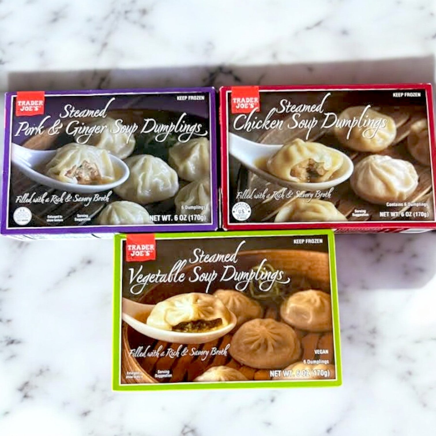 Three boxes of Easy Lunches' 3 Pack Dumpling Combo on a marble surface, featuring Pork & Ginger, Chicken, and Vegetable steamed soup dumplings, each offering a taste of Asian cuisine.