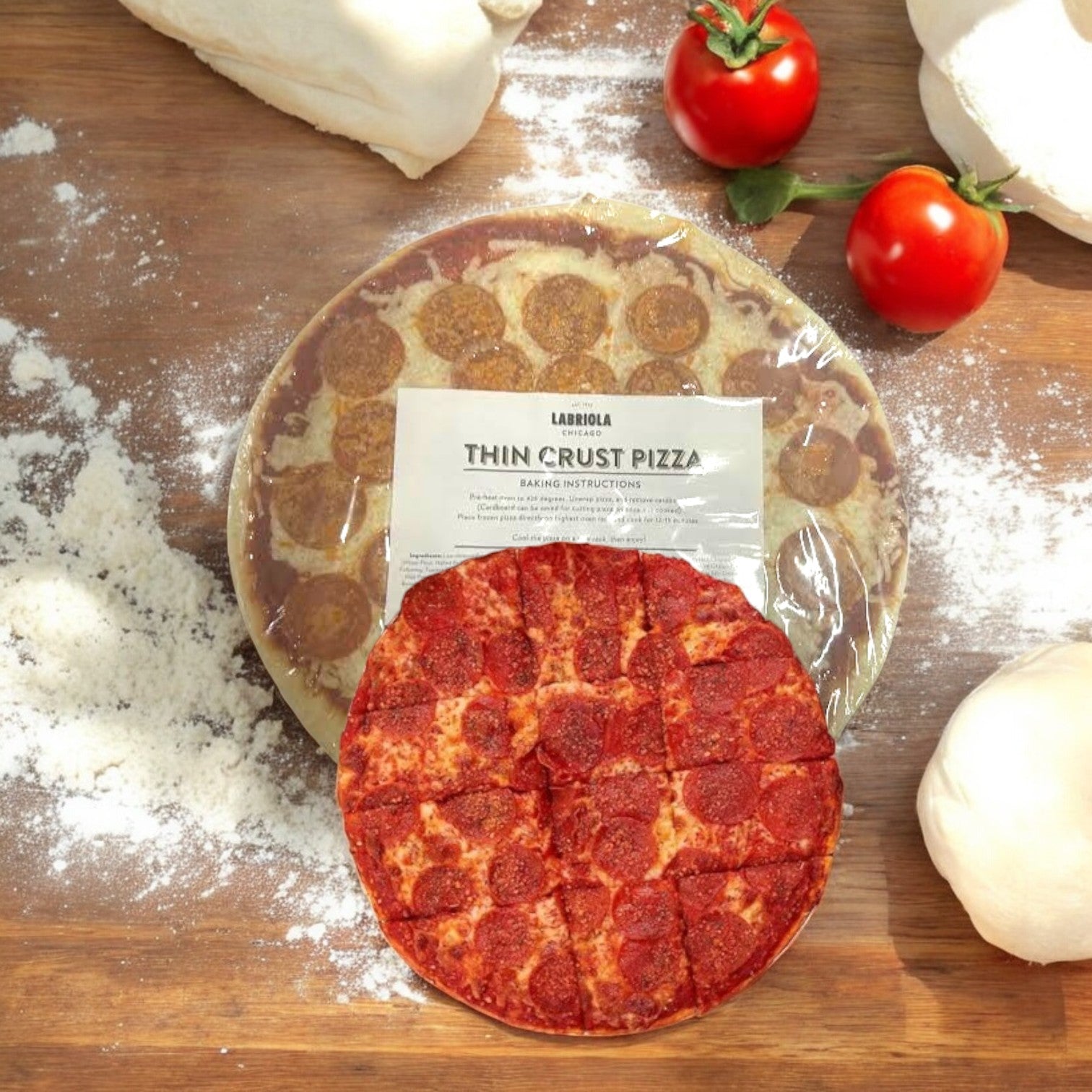 A Labriola Chicago pizza sits on a wooden surface, its thin crust topped with pepperoni. Flour, dough, and ripe tomatoes surround this Labriola Chicago Pepperoni Thin Crust Pizza-1 Count to create a rustic scene.