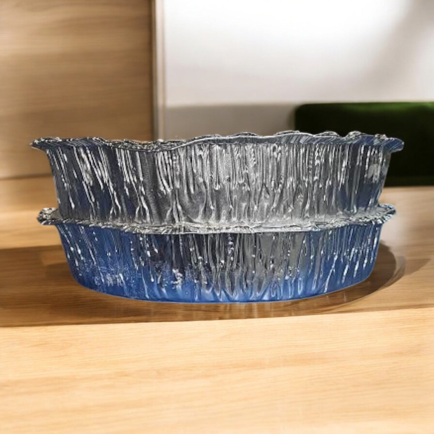 A transparent, textured glass bowl with a wavy rim rests on wood, resembling Pequod Pizza's artistic presentation with their Deep Dish Pizza 2-Pack Combo: Cheese & Pepperoni.