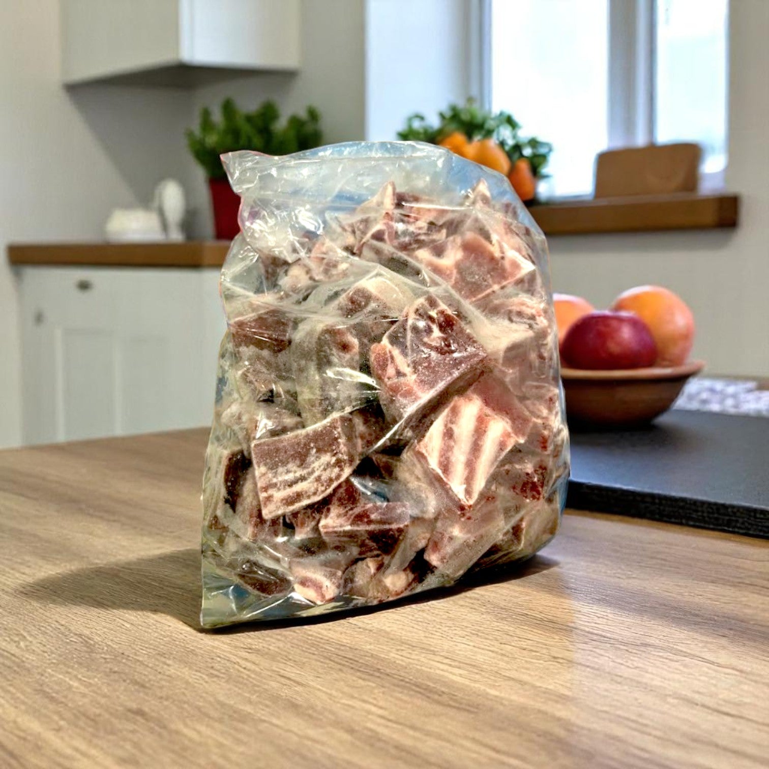 A plastic bag of marbled chocolate sits on a wooden kitchen counter next to a case of Restaurant Depot Halal Goat Cubes-15lbs-Frozen, with fruit and plants visible in the background.