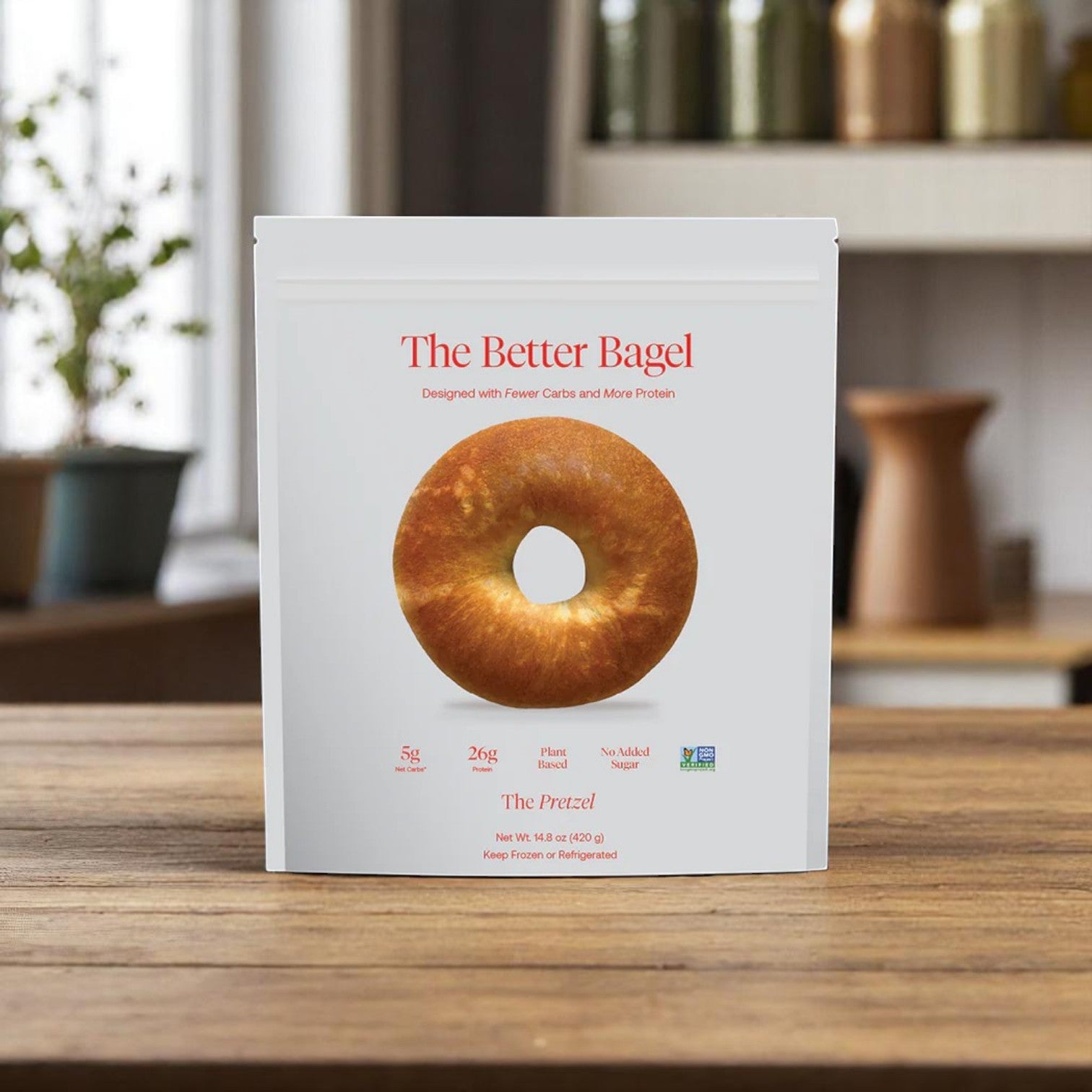 A white package labeled "BetterBrand, The Better Bagel – Pretzel Style" with a bagel image rests on a kitchen table—offering a high-protein, nutritious choice for your morning. Available in 1 bag (4 bagels), in stock and ready to ship!.
