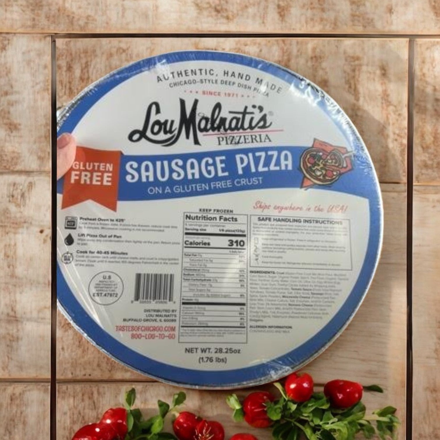 Lou Malnati's Gluten Free Crust Combo Pack, which includes three of their famous deep dish pizzas with sausage, is placed on a wooden surface accented by red cherry tomatoes and fresh basil leaves.