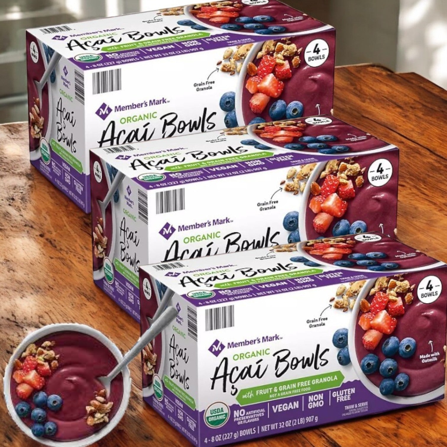 Three boxes of Member's Mark Organic Acai Bowl, Frozen, 4 Ct sit on a wooden table. These premium products are certified organic, vegan, non-GMO, and gluten-free, offering both affordability and excellent nutrition for your lifestyle.