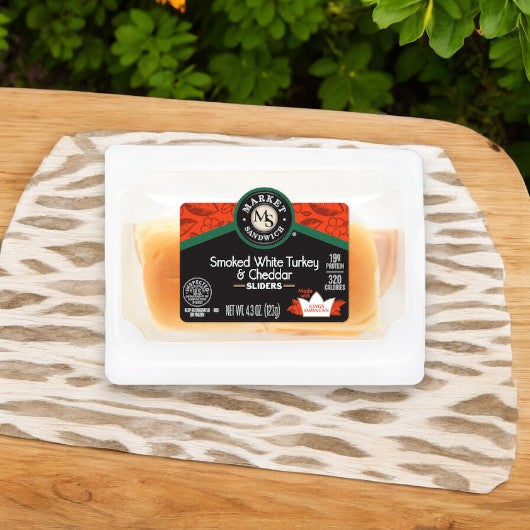 E.A. Sween's Smoked White Turkey and Cheddar Sliders, nestled in mini buns, are artfully arranged on a zebra-patterned surface with lush green foliage. Ships frozen with a 30-day shelf life in the cooler!.