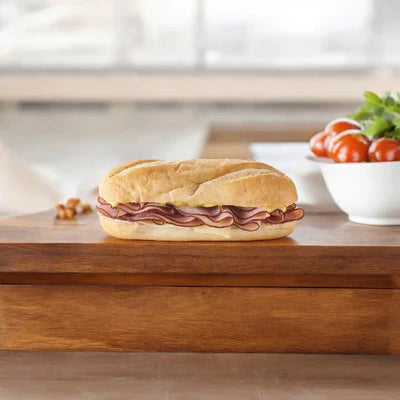 A sliced deli meat sandwich filled with premium ingredients lies on a wooden board. A bowl of cherry tomatoes and lettuce is visible in the background, creating the ideal grab-and-go lunch option. Enjoy E.A. Sween’s Sandwich Combo 5 Items—a delicious variety pack perfect for any meal!.