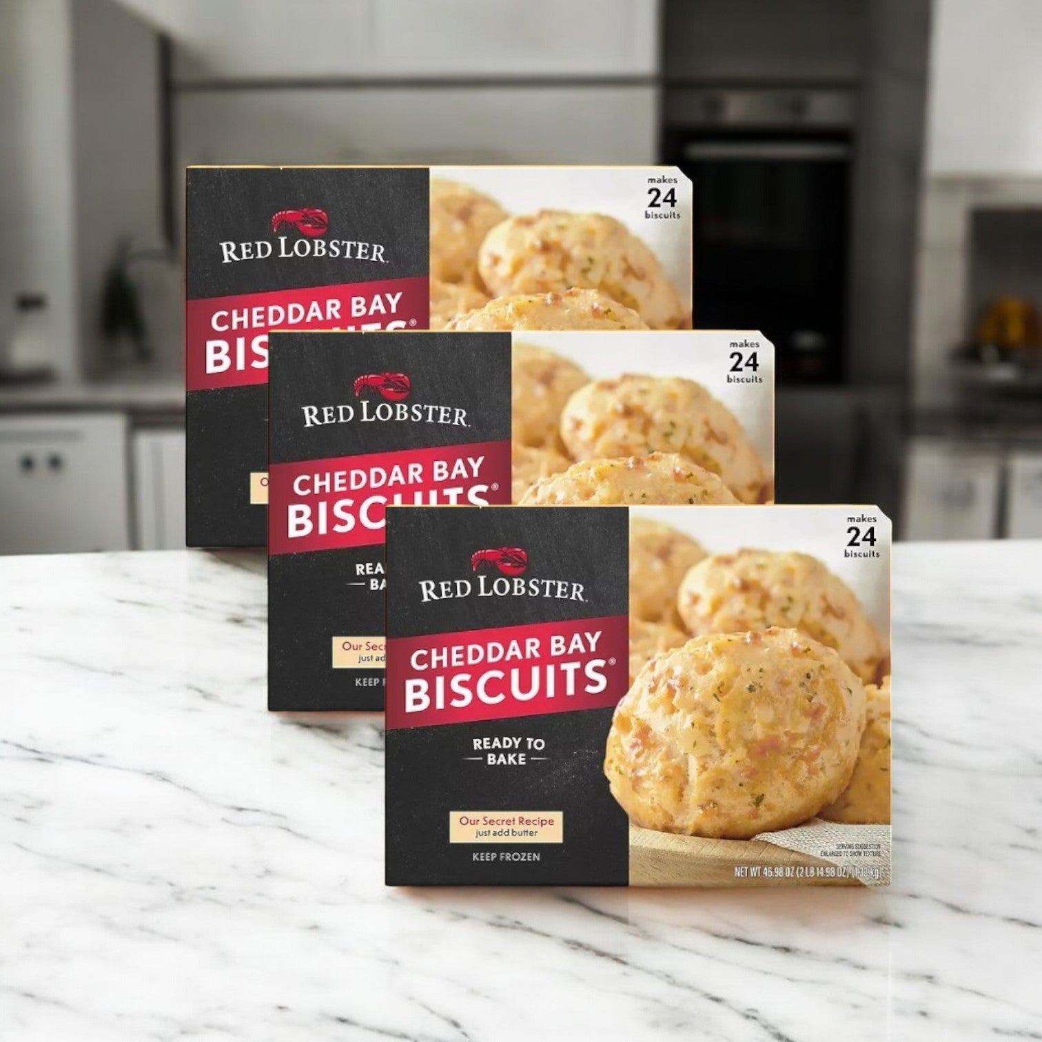 Three cases of Red Lobster's Frozen Cheddar Bay Biscuits, 24-count each, are displayed on a marble countertop, showcasing these beloved restaurant recipe biscuits in a cozy kitchen setting.