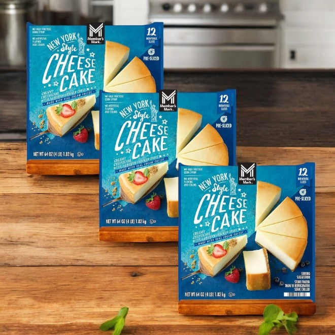Three boxes of Member's Mark New York Style Cheesecake by Member's Mark, each containing twelve pre-sliced pieces with a graham cracker crust, are showcased on a wooden surface in a cozy kitchen setting.