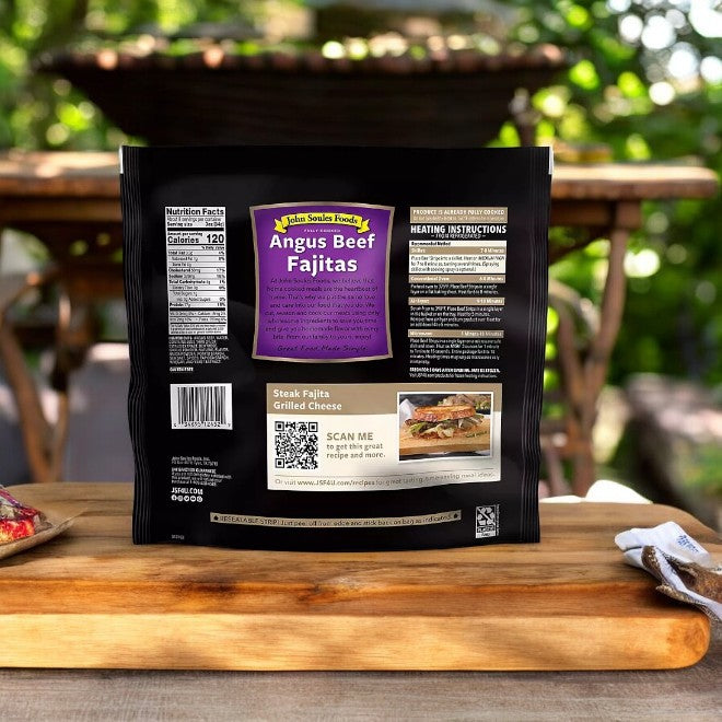 A package of John Soules Fully Cooked Angus Beef Fajitas, 24 oz, sits on wood with nutrition facts, prep instructions, and a recipe QR code. Ready-to-heat against an outdoor scene with blurred greenery in the background.