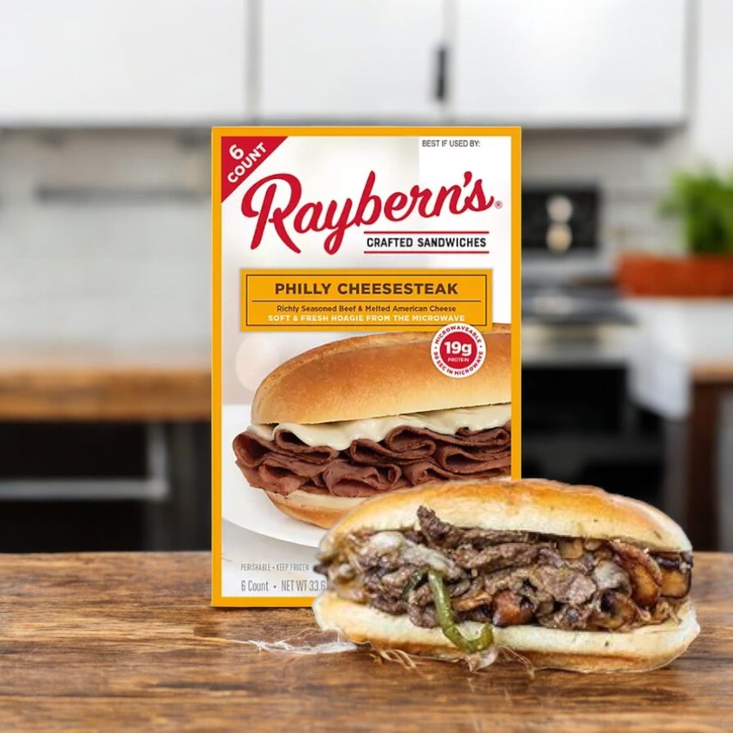 A box of Raybern's Philly Cheesesteak Crafted Sandwiches (Frozen, 6 count) sits on the table, showcasing a cooked sandwich with juicy beef and vibrant green peppers, perfect for those craving flavorful frozen sandwiches.