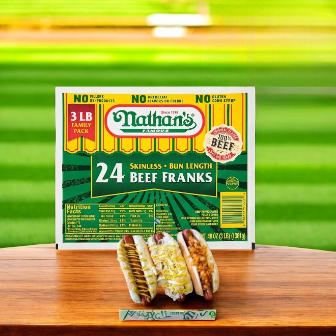 A box of Nathan's Famous Beef Franks- 1 Count- 24 Beef Franks rests on the table, featuring two grilled 100% beef hot dogs in buns with condiments, set against a soft, blurred background.