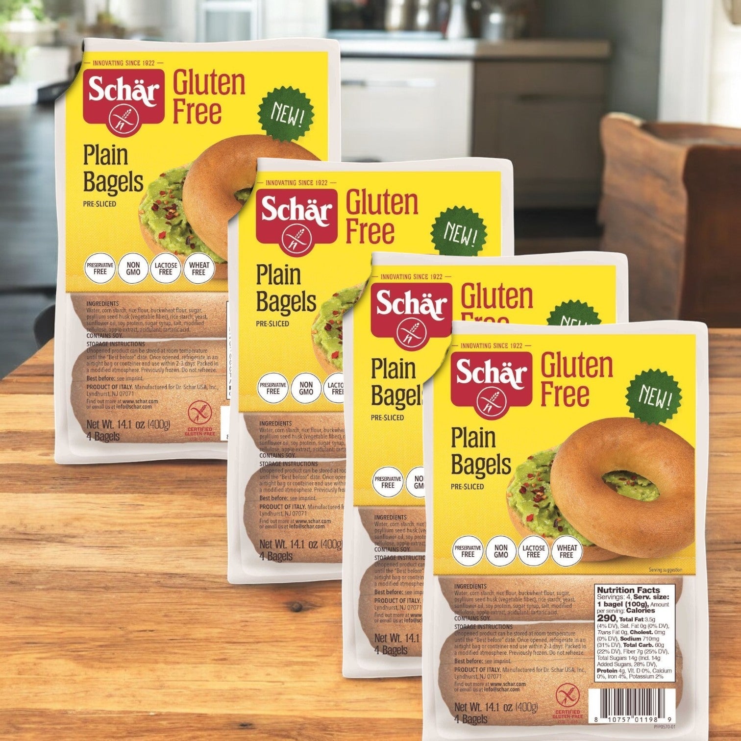 Four Schar Gluten Free Plain Bagel packages, each 14.1 oz. and in a set of 4 per case, are beautifully displayed on a wooden surface in a cozy kitchen, ideal for those with gluten sensitivities.