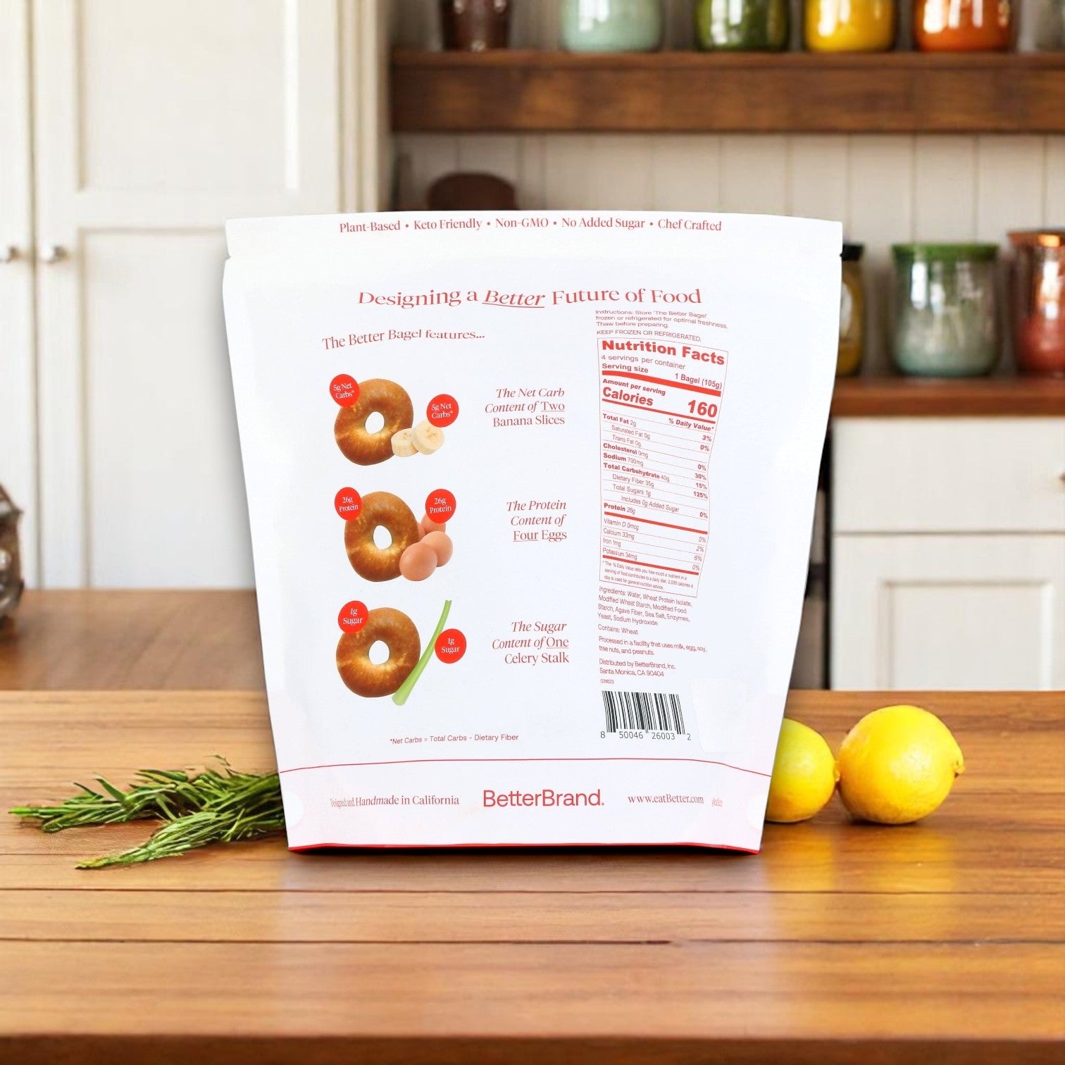 A bag of BetterBrand, The Better Bagel – Pretzel Style (1 bag, 4 bagels) sits on a wooden kitchen counter, highlighting nutrition facts and features. Lemons, rosemary, and jars decorate the background. In stock—ready to ship!.
