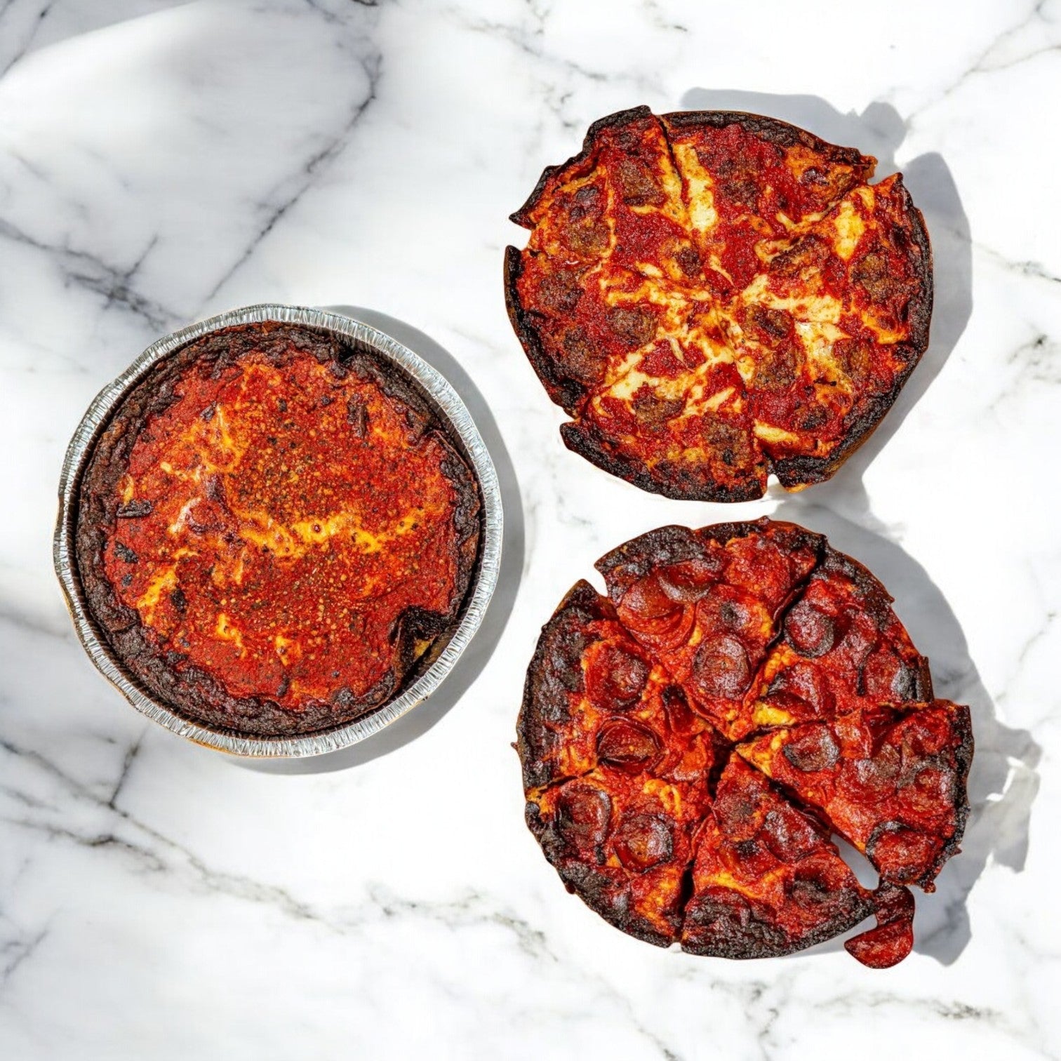 A trio of Pequod's Deep Dish Pizzas—Cheese, Pepperoni, and Sausage—sit enticingly on a marble surface. This 3-Pack Combo from Pequod Pizza bursts with rich, legendary Chicago-style flavors and savory toppings, with free shipping!.