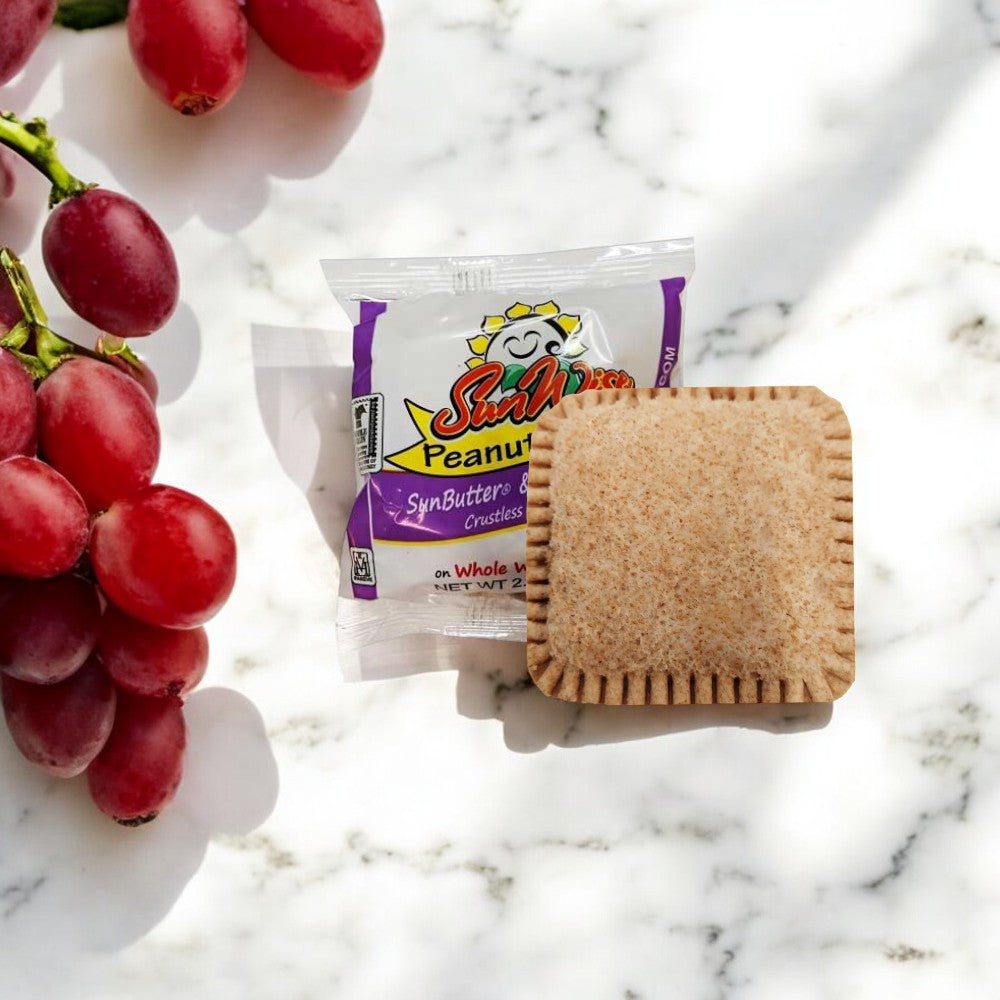 A SunWise Grape Jelly Sandwich from the Sunwise brand rests on marble alongside red grapes, offering a delicious nut-free snack option.