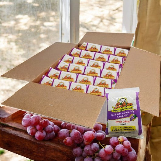 A table holds an open box with Sunwise Individually Wrapped Sunbutter & Grape Sandwiches, allergen-friendly and peanut-free. A small bag of grapes in front complements this tasty treat for those seeking Sunbutter options.