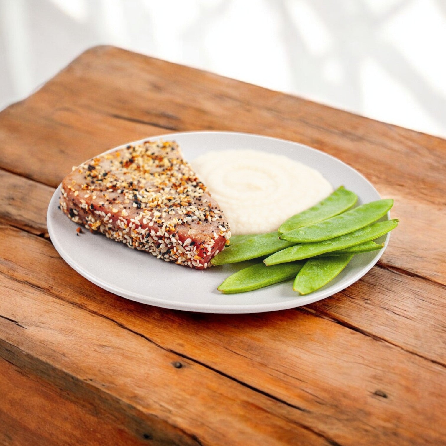 A wooden table displays Portico Imperial by Sysco Yellowfin Tuna Steak with mashed potatoes, sugar snap peas, and individually quick frozen tilapia fillets.