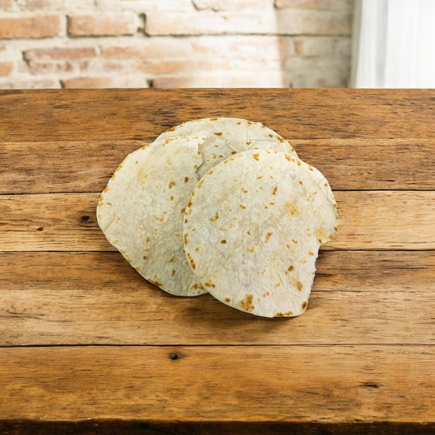 Two El Milagro White Flour Tortillas (5-Inch, from a 42-pack of 1 dozen) are stacked on a wooden table with a brick wall behind. This item ships on Mondays—plan accordingly!.