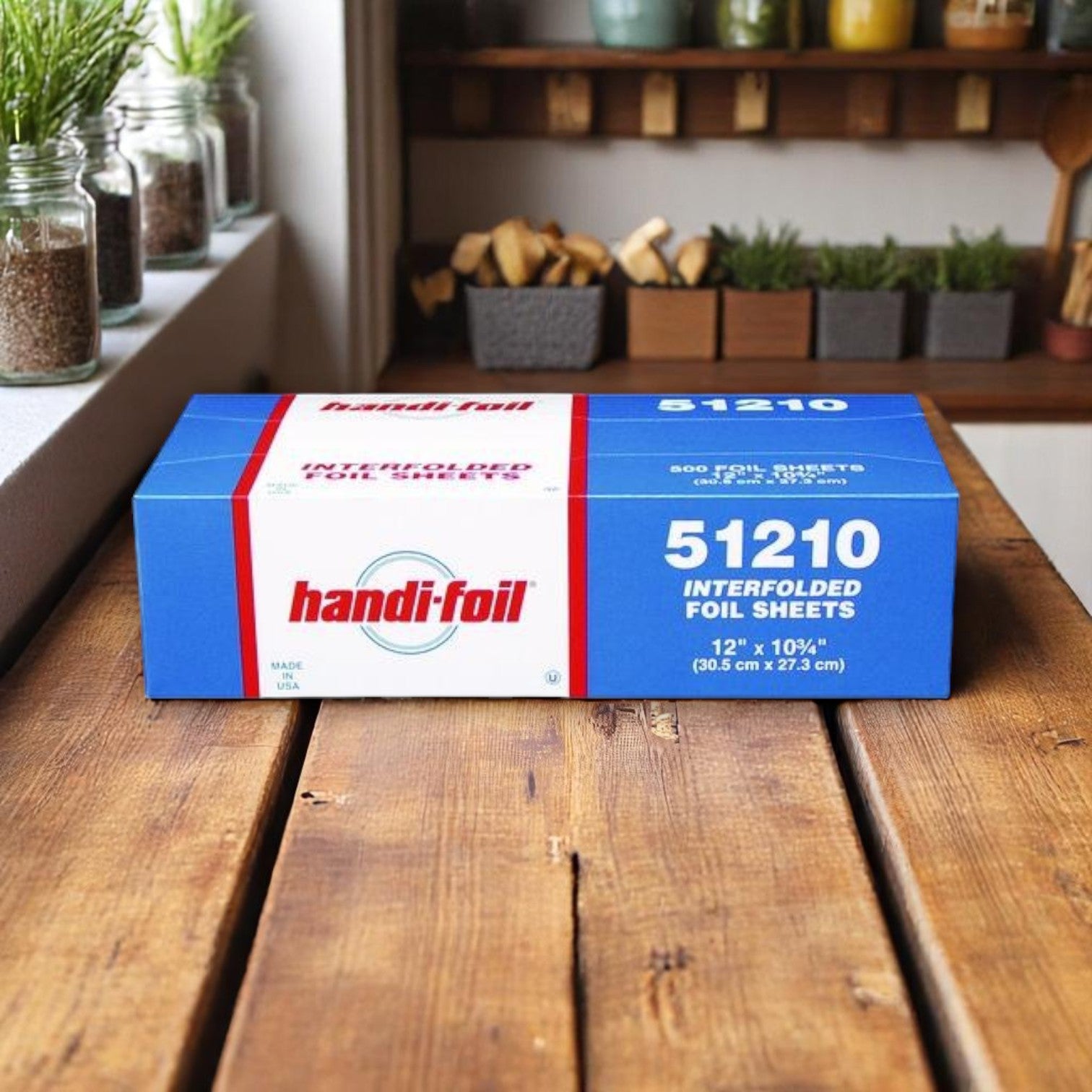 A box of Handi-Foil of America HFA Pre-Cut Foil Sheets, 12" x 10.75", 500 sheets (51210), rests on a wooden table in a cozy kitchen.