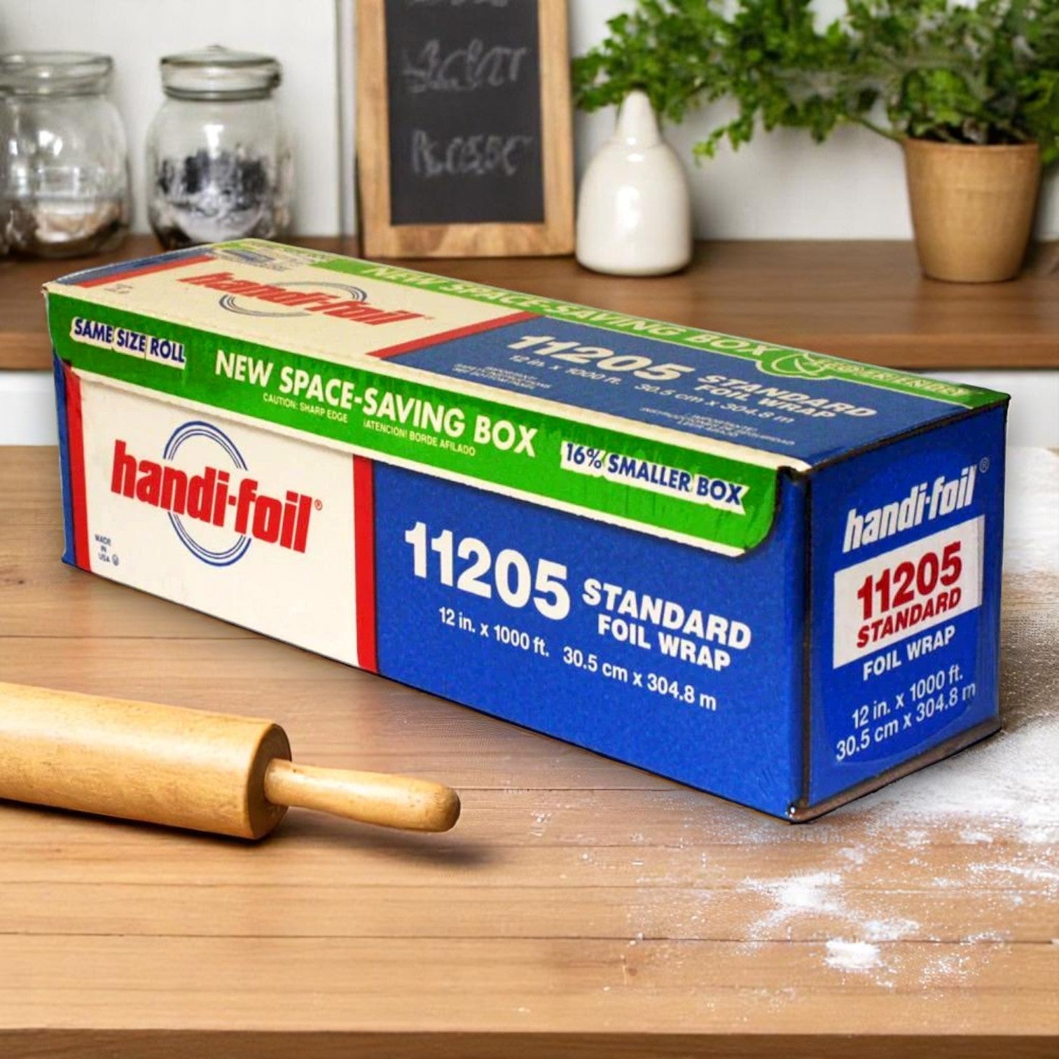 A box of Handi-Foil of America HFA 12" x 1000' Standard Weight Foil Roll – Commercial Grade sits on a kitchen counter beside a rolling pin and scattered flour.