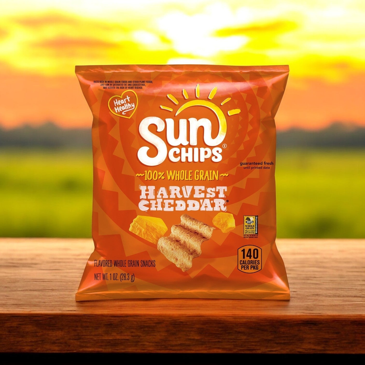 A Sun Chips Multi-Grain Harvest Cheddar Chips 104/1 oz bag rests on wood, its cheesy flavor highlighted against a blurred outdoor scene.