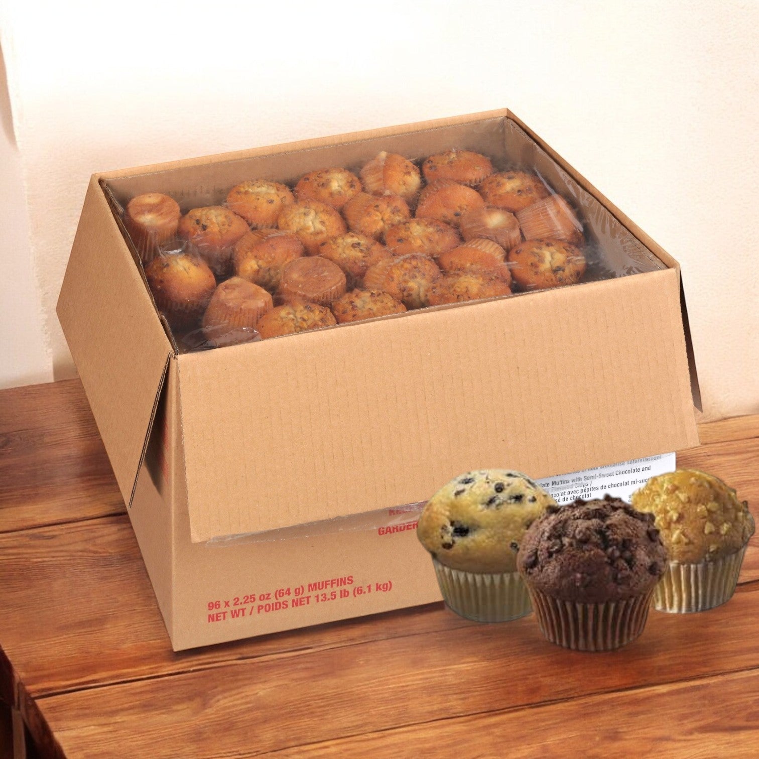 An Otis Spunkmeyer Muffin Variety box, containing blueberry, banana, and chocolate chip muffins (96/2.25 oz), is open on the wooden table.