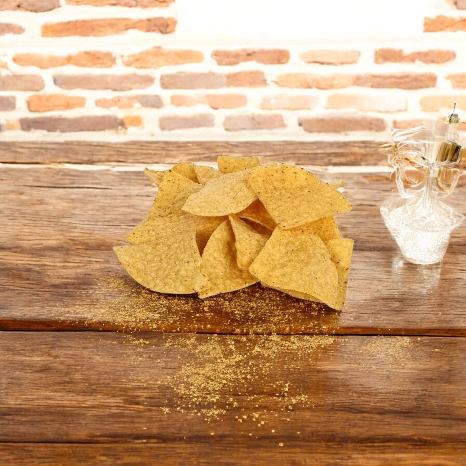 A wooden table holds a pile of El Milagro Corn Tortillas 4-Way Precut Homestyle, next to a small clear container. A brick wall backdrop enhances the authentic vibe.