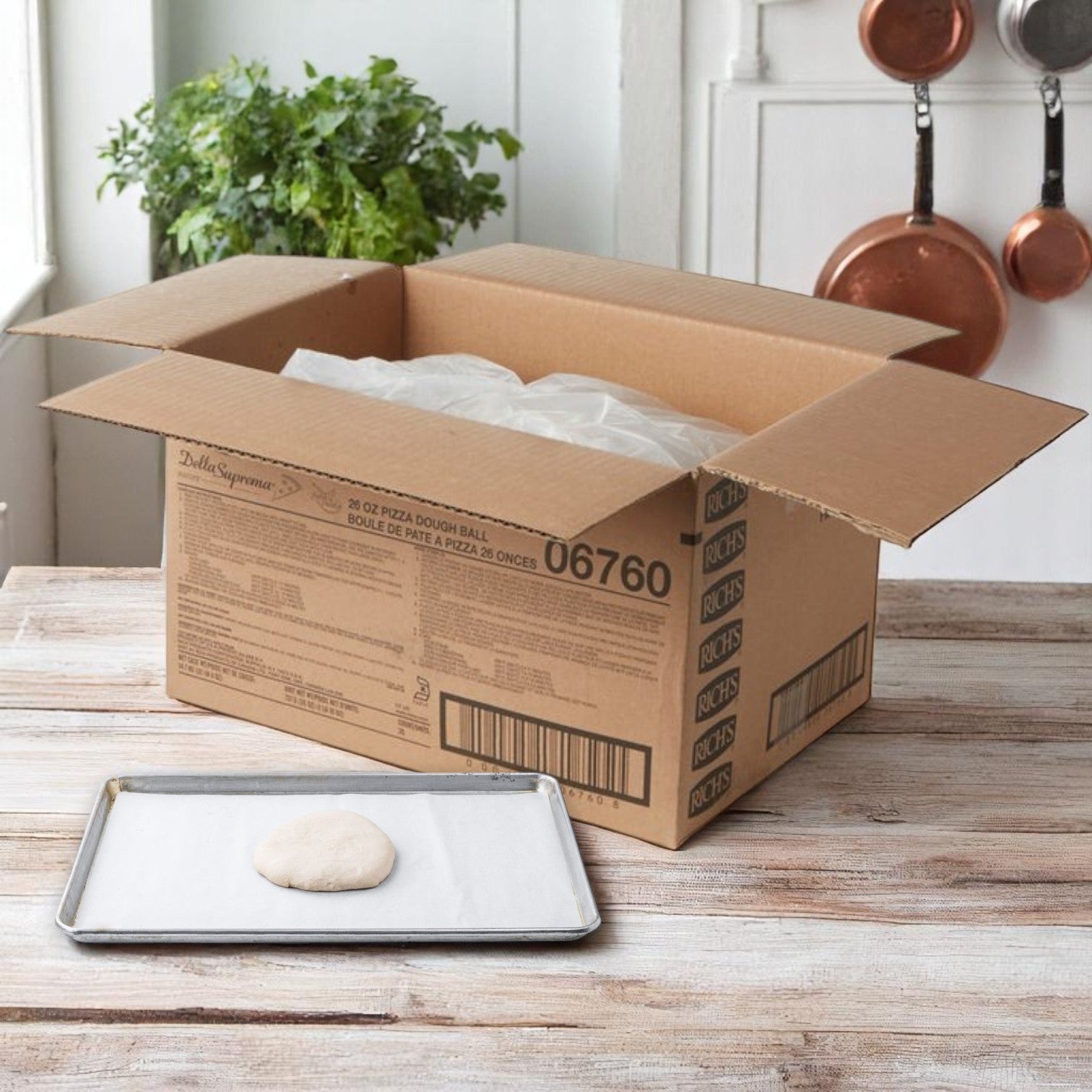 A cardboard box sits open on a table near a window; in front, a metal baking tray holds a single Rich’s Pizza Dough Ball (26 oz. from the 20-count bag), perfectly crafted for authentic pizzeria-style pizzas, on parchment paper.