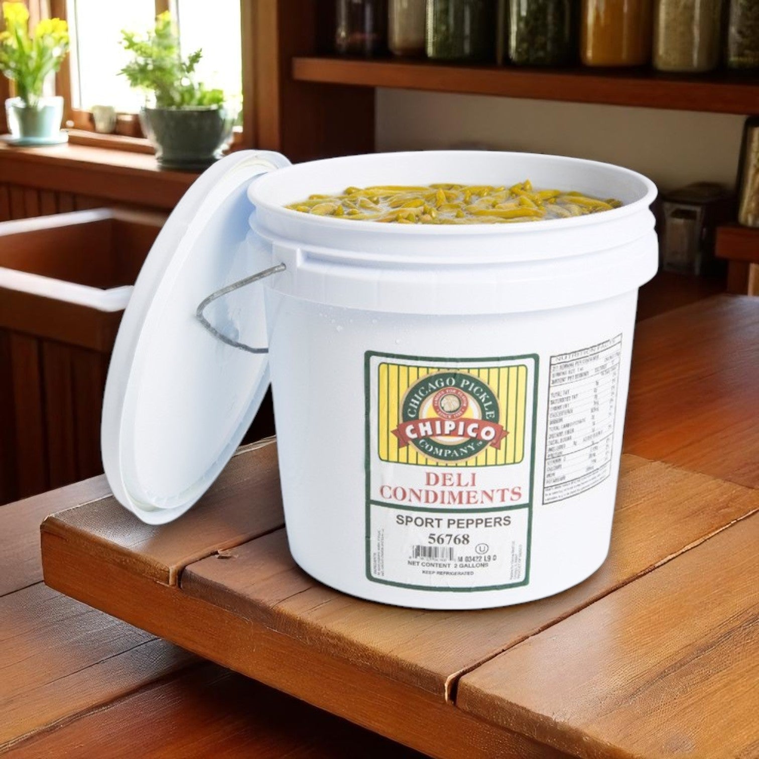 A 2-gallon container of Vienna Beef Chipico Mild Sport Peppers sits open on a wooden kitchen counter, ready to add authentic pickled green chiles to Chicago-style hot dogs.
