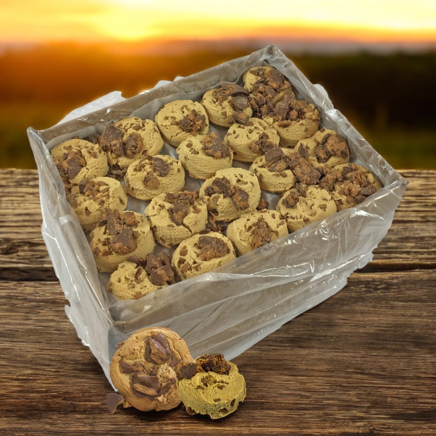 A tray of David's Cookies Reese's Peanut Butter Chunk cookie dough wrapped in plastic sits on a wooden surface outdoors at sunset, evoking warm, nostalgic aromas.