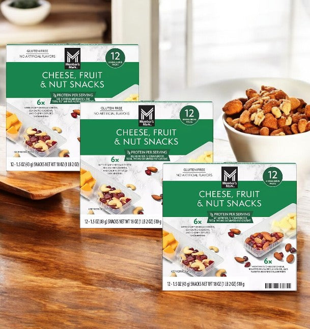 Three cases of Member's Mark Cheese, Fruit, and Nut Snacks, each containing twelve 1.5 oz packages, are attractively arranged on a wooden table with a bowl of mixed nuts in the background—ideal for satisfying cravings healthily.
