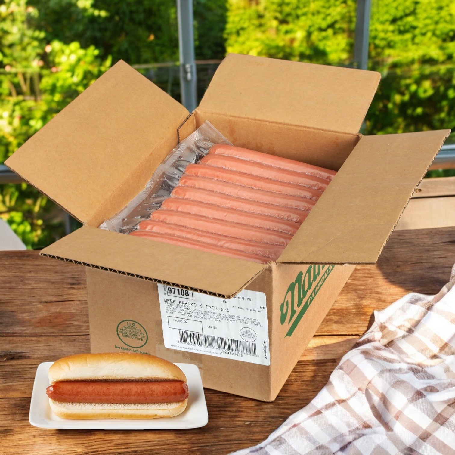 On the table lies an open box with multiple packs of Nathan's Frankfurter All-beef, 6"-50 Franks A Case by Nathan's Famous, and one grilled all-beef frankfurter in a bun on a small plate nearby.