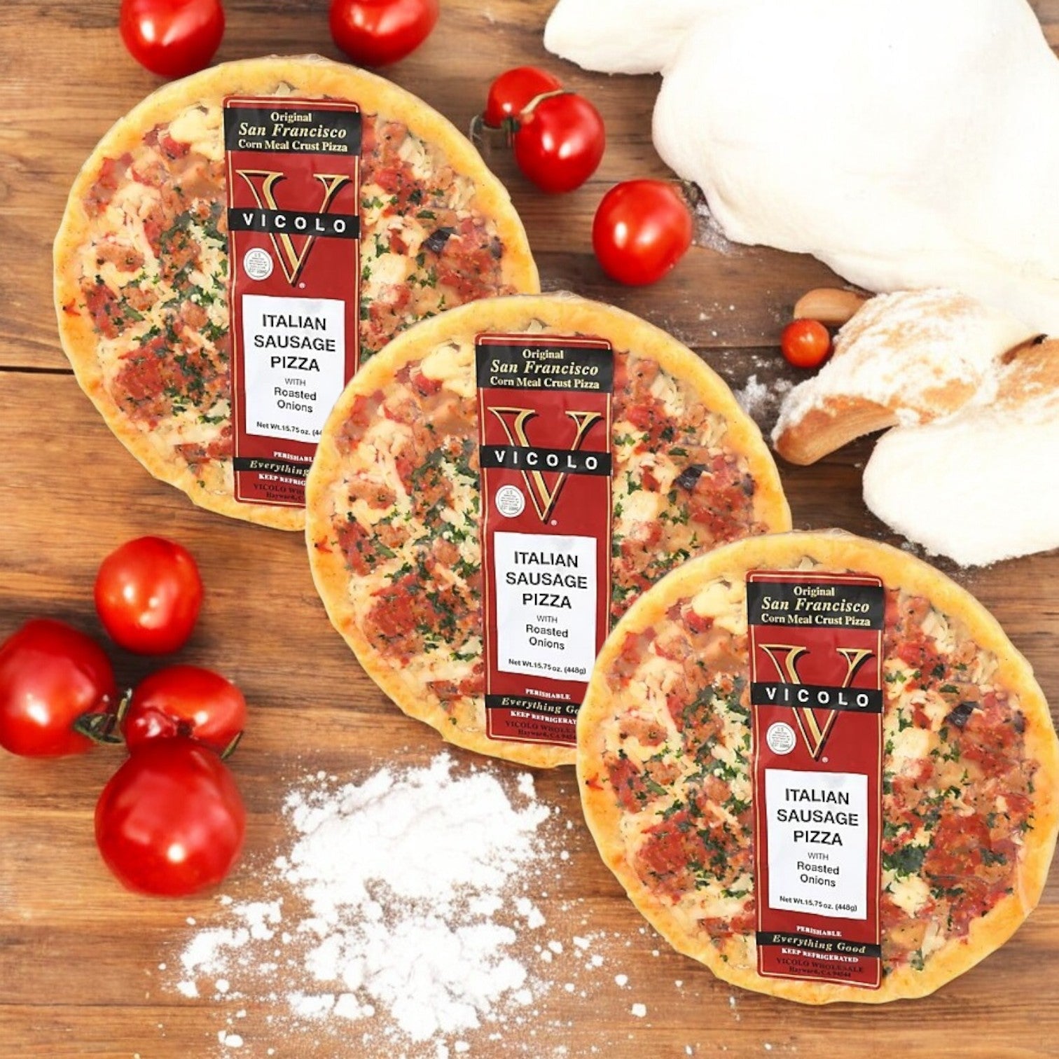 Three Vicolo Italian Sausage Pizzas are displayed on a wooden surface with flour, fresh tomatoes, and dough in the background. The crispy crust and generous mozzarella cheese layer promise an irresistible taste sensation.