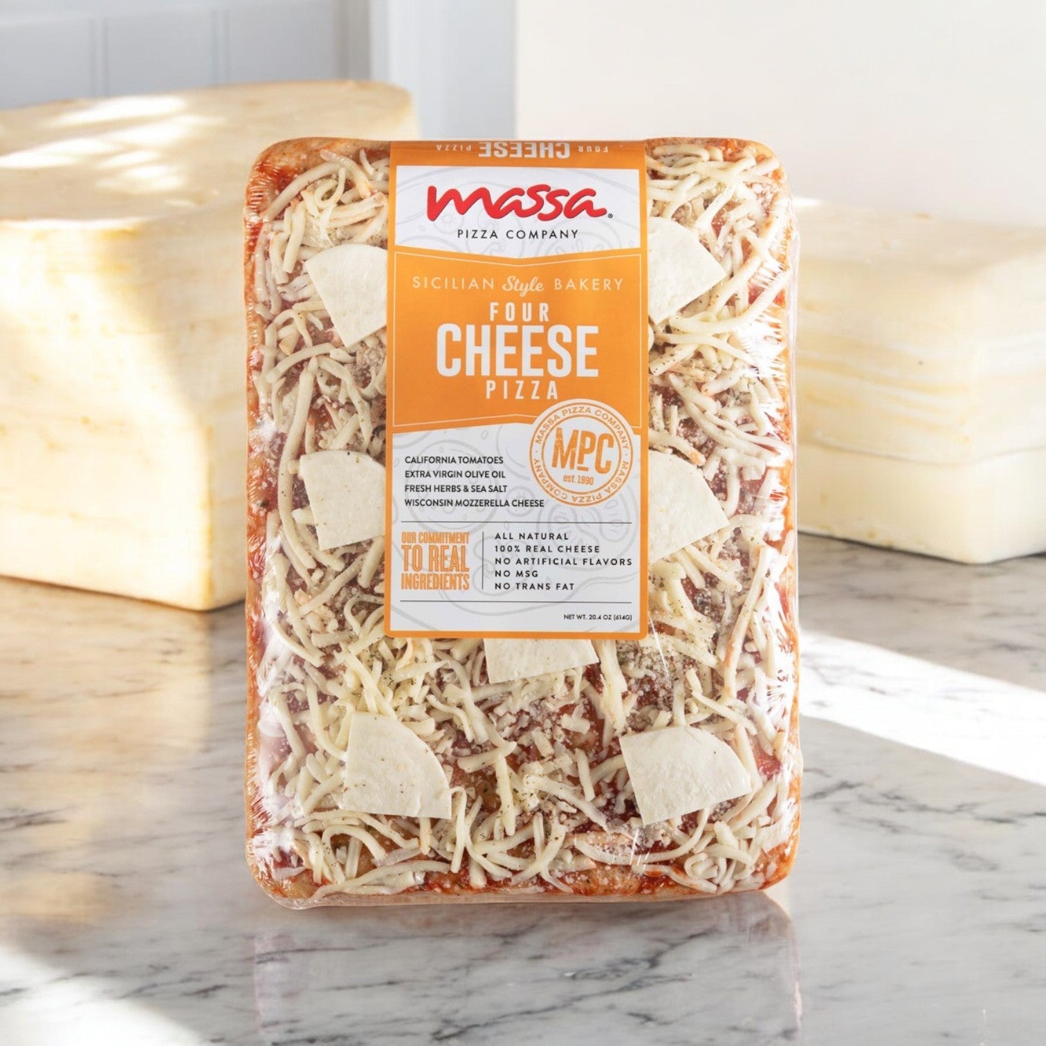 On a marble countertop sits the packaging of Massa Pizza Co. Four Cheese Sicilian Bakery Pizza, 23.1 oz., prominently displaying labels from "Massa Pizza" and "Sicilian Style Bakery," and featuring an artisan bakery crust made with all-natural ingredients.