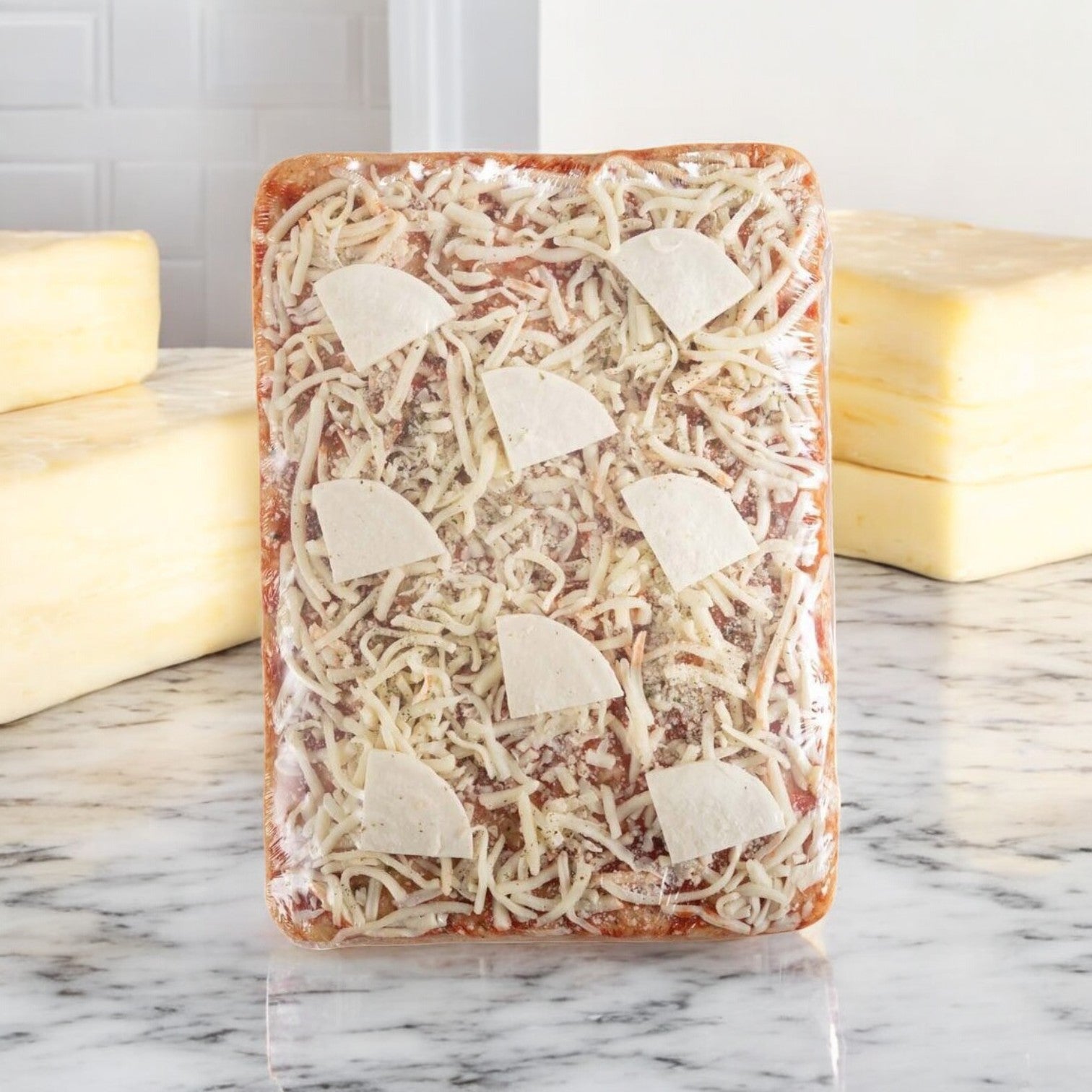 Massa Pizza Co. Four Cheese Sicilian Bakery Pizza, weighing 23.1 oz., rests on a marble counter, featuring an artisan crust from Massa Pizza. It's topped with shredded cheese and sliced toppings crafted from all-natural ingredients.