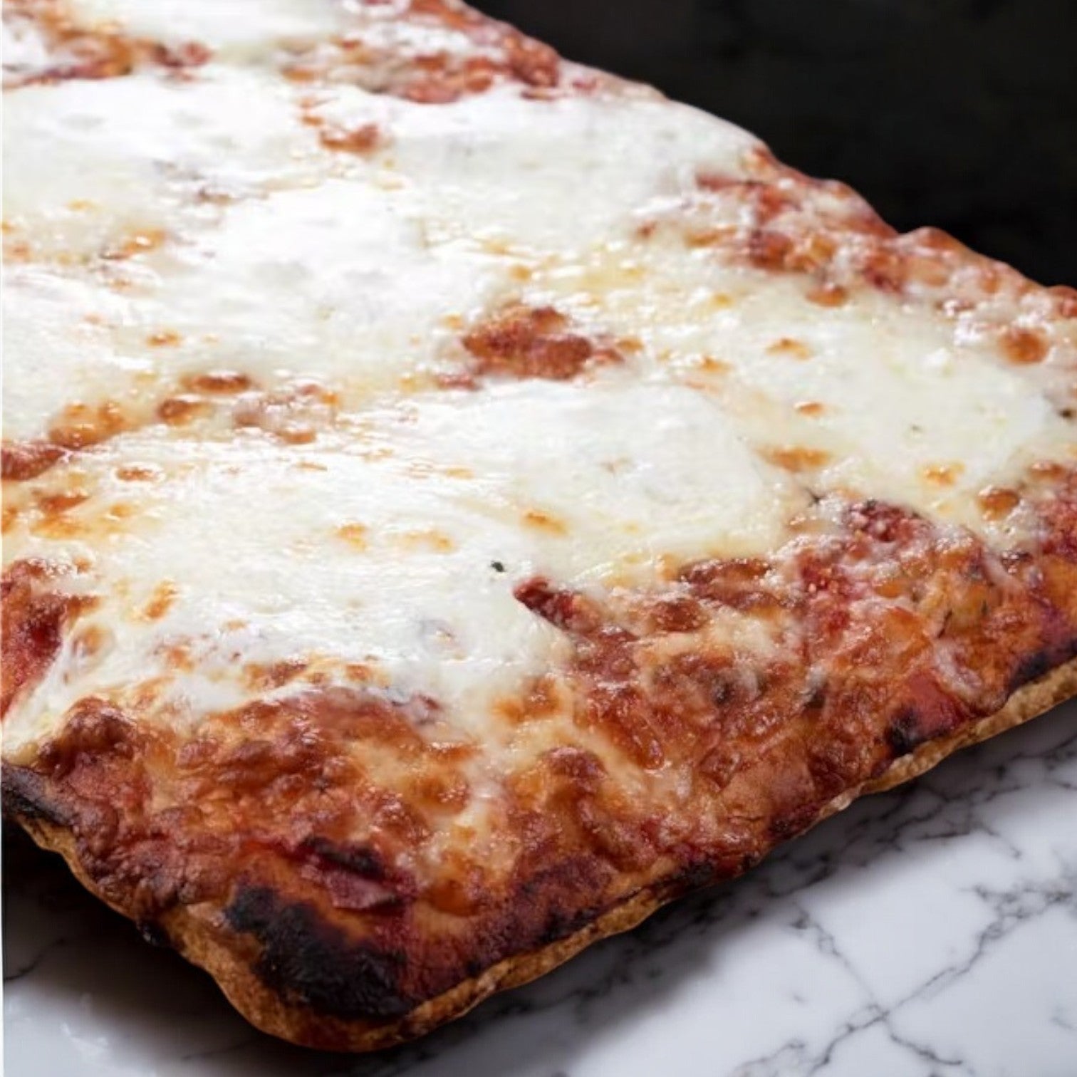 On a marbled surface sits a rectangular Massa Pizza Co. Four Cheese Sicilian Bakery Pizza, featuring an artisan bakery crust crafted with all-natural ingredients.