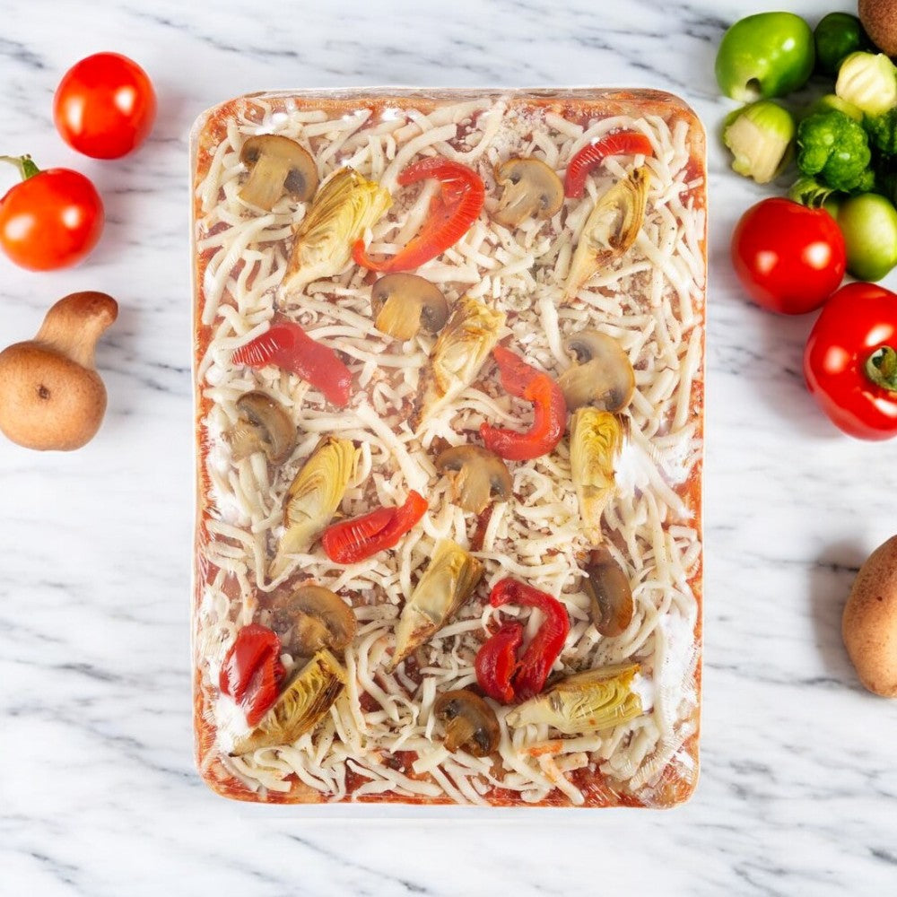 The Massa Pizza Co. Roasted Veggie Sicilian Bakery Pizza, a 23.1 oz masterpiece by Massa Pizza, showcases a delightful mix of mushrooms, red peppers, and artichokes on handcrafted dough. Elegantly displayed on a marble surface, it is surrounded by fresh tomatoes, mushrooms, and Brussels sprouts for an enticing presentation.