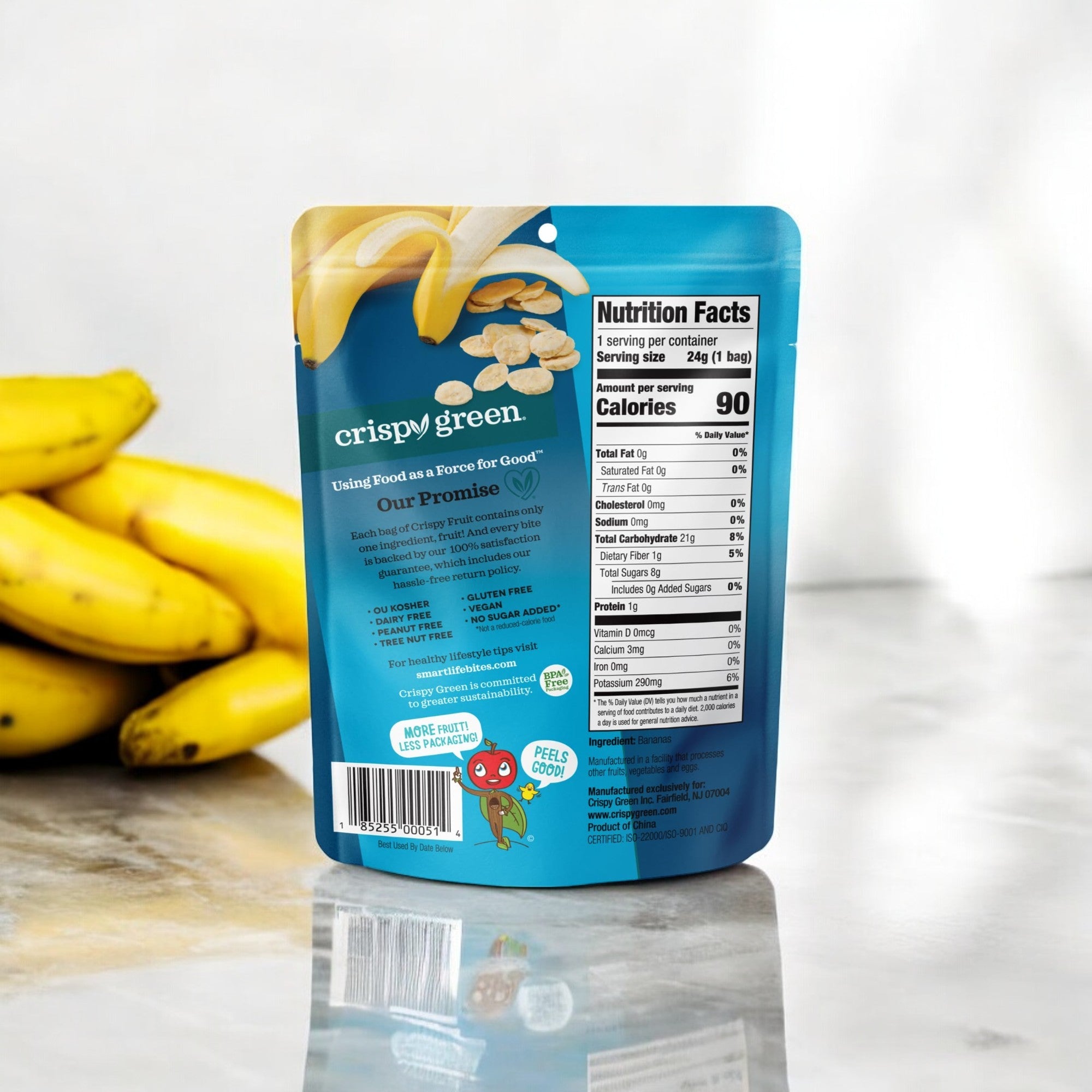 On the countertop is a blue package of Crispy Fruit All Banana, 0.85 oz -1 Count, with clear nutrition facts. Yellow bananas offer a fresh backdrop in this scene of sustainable snacking delight, inviting exploration of Crispy Green Pineapple Slices' tropical allure.