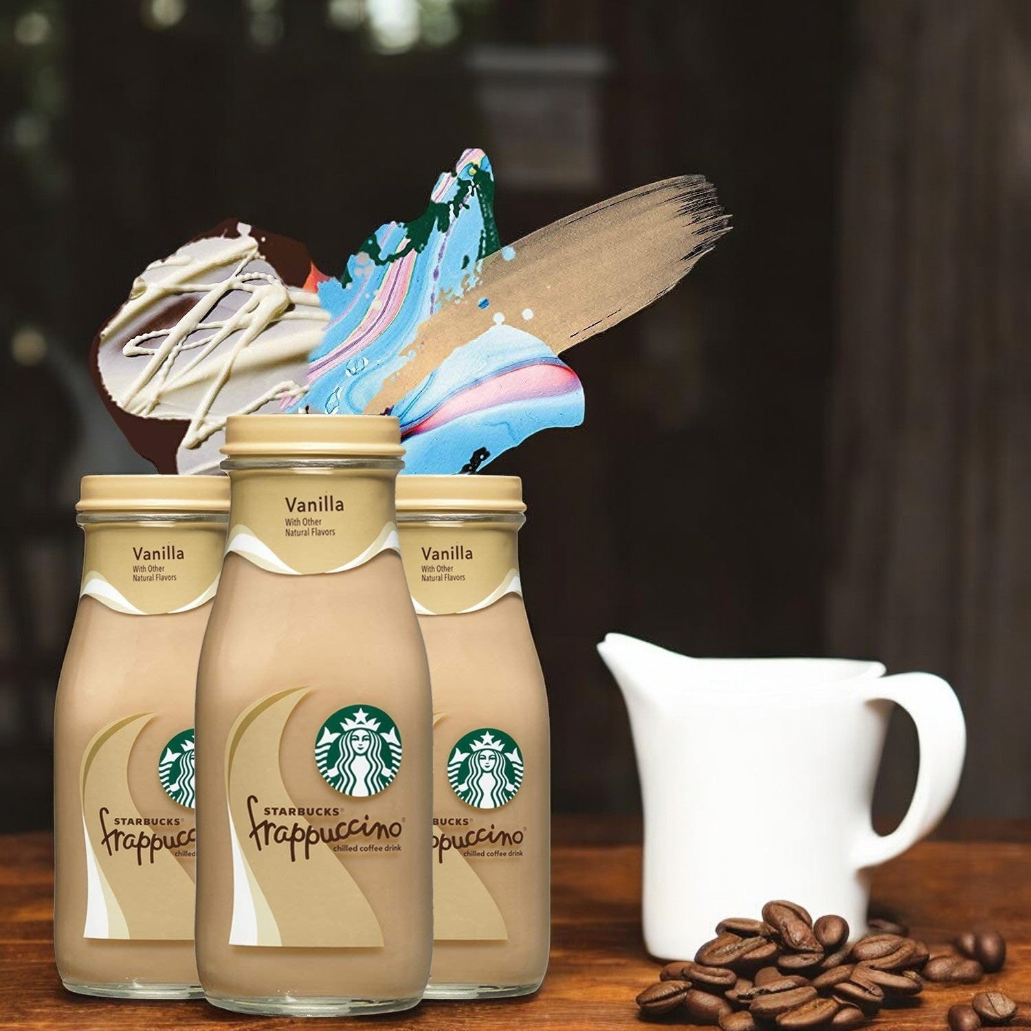 Three cases of Starbucks Frappuccino Vanilla Coffee 15ct are surrounded by abstract paint splashes, with a white jug and scattered coffee beans on the wooden surface, capturing the delightful vanilla coffee essence.
