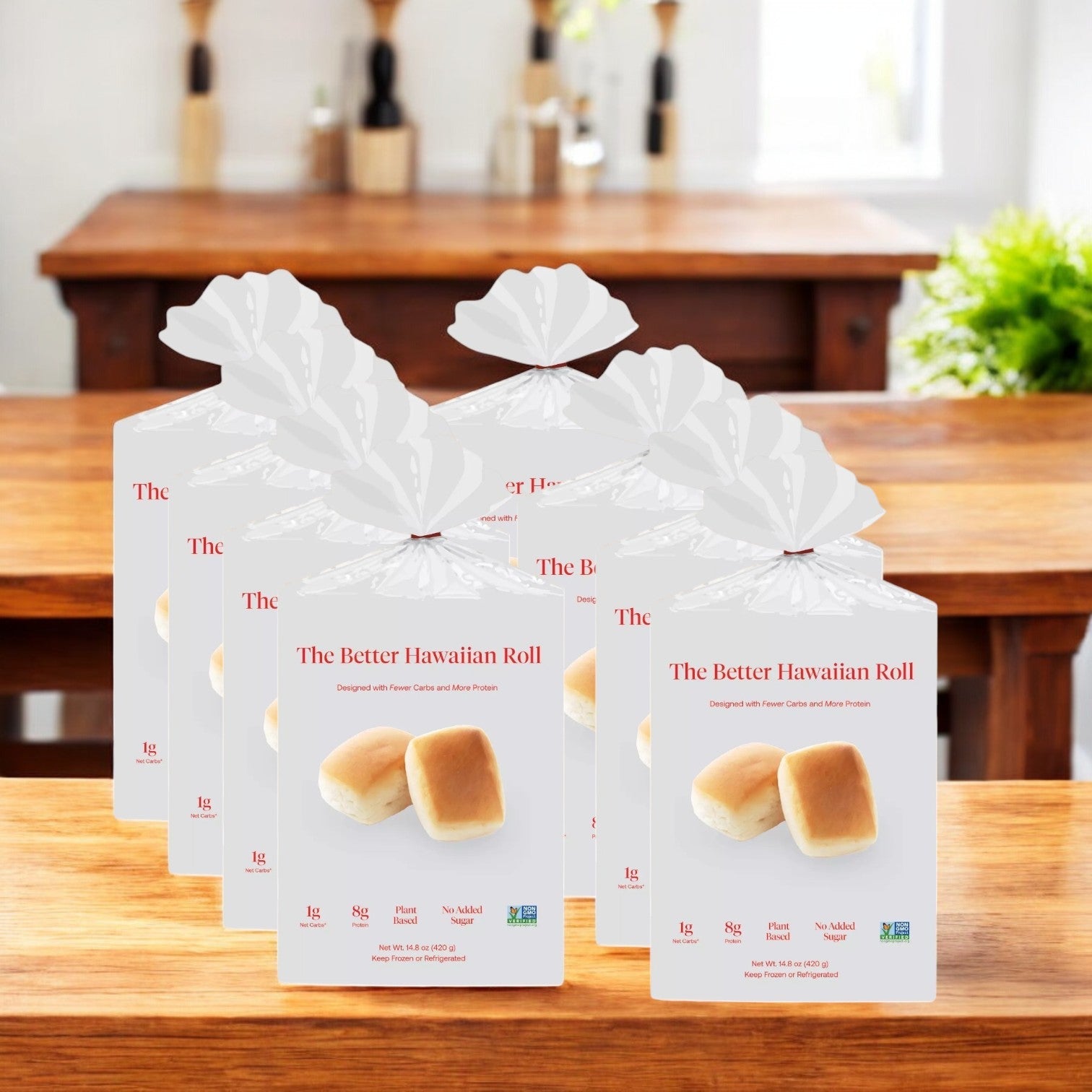 The Better Hawaiian Roll" by BetterBrand, in packs of 12 (8 bags total), sits on a wooden table. Each package features images of two fluffy rolls and nutritional info against a blurred kitchen background. In stock and ready to ship!.