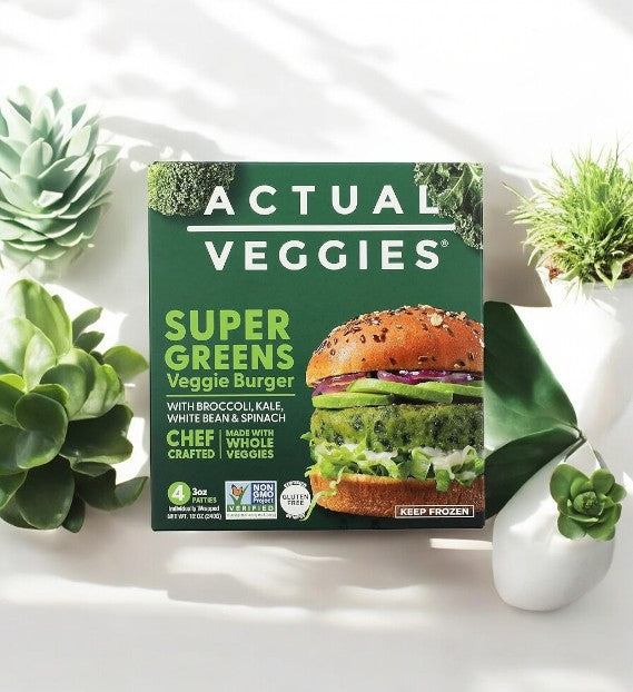 The Actual Veggies Super Greens Veggie Burger-1 Count sits among green succulents, showcasing its label with broccoli, kale, white beans, spinach, and a "keep frozen" notice.