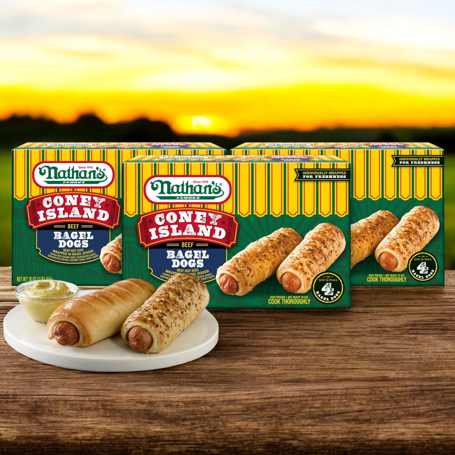 Nathan's Famous Coney Island Bagel Dogs – 20 oz. - 3 Count are showcased with two cooked bagel dogs on a plate upfront, featuring premium beef hot dogs against a picturesque sunset backdrop.
