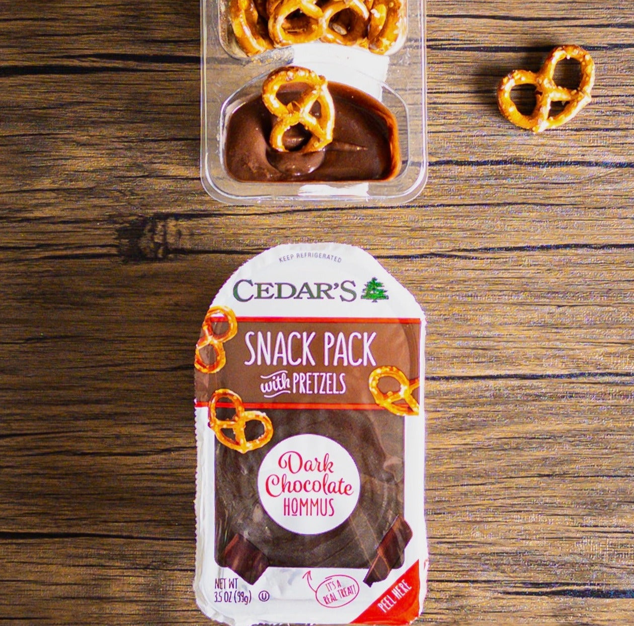 An open container of Cedar's Snack Pretzels with Chocolate Hommus is elegantly displayed on a wooden surface.