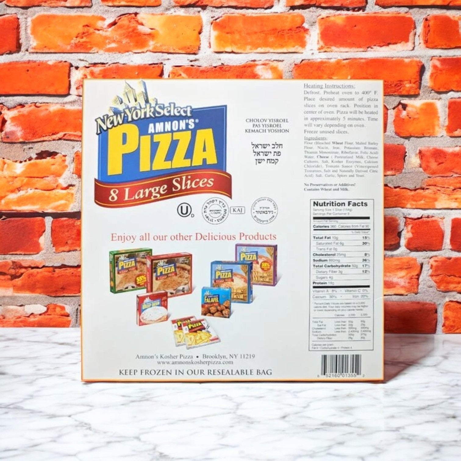 A New York Select Amnon's Kosher Pizza 55% Reduced Fat Frozen 36 oz.- 3 Count box against a brick wall displays product details, heating instructions, and nutrition facts. The design showcases various pizza varieties at the bottom, promoting a healthier pizza option.