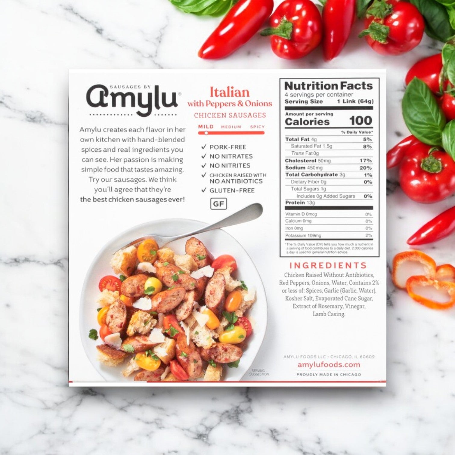 A 9 oz box of Amylu Italian Chicken Sausage with Peppers & Onions rests on a marble surface, surrounded by fresh ingredients. The packaging highlights its gluten-free feature and displays nutritional information and an ingredients list.