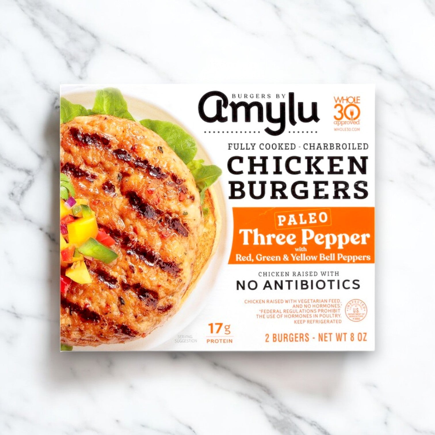 The packaging for Amylu Paleo Three Pepper Chicken Burgers (8 oz) displays a charbroiled burger with peppers and emphasizes "Paleo," "Three Pepper Blend," and "No Antibiotics." It's gluten-free and includes two burgers.