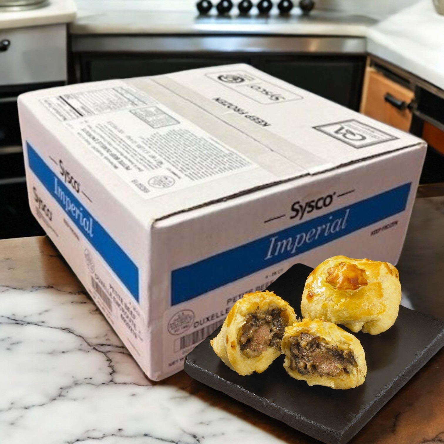 On a kitchen counter is a Sysco box labeled "Beef Wellington- Deluxe- Sysco Appetizer," with three pastry-wrapped beef samples on a black plate, their flaky puff pastry promising the perfect premium appetizer.