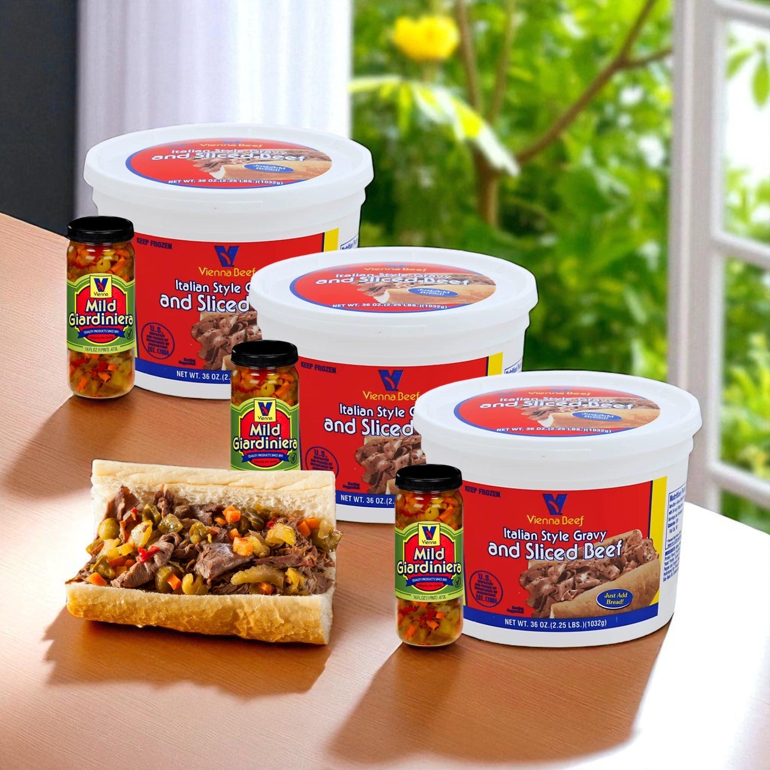 Three Vienna Beef Italian Style Gravy and Sliced Beef 36oz containers, plus three jars of mild Vienna Giardiniera, sit on a table near the window with greenery outside.