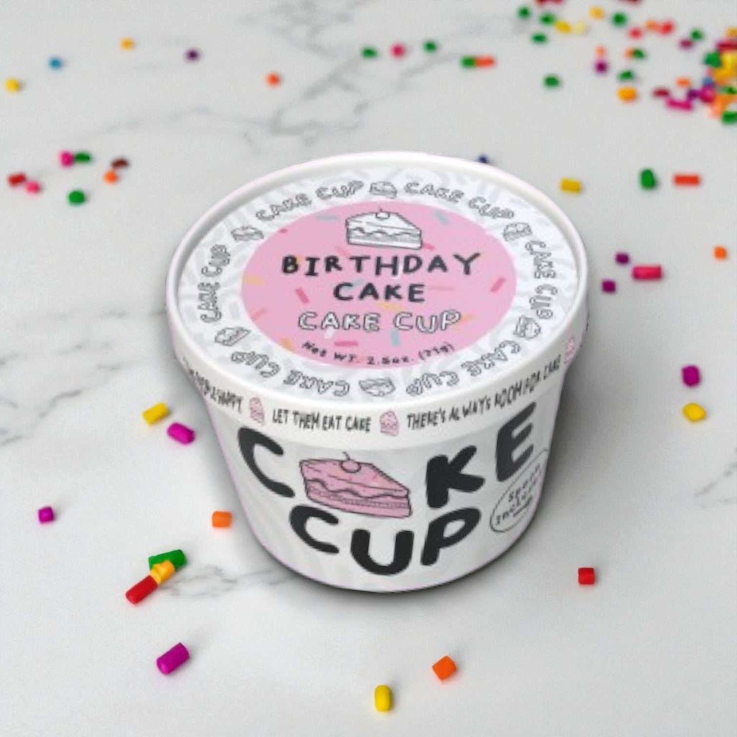 A 2.5 oz Eat Cup Cake, Birthday Cake Dessert Cup by Eat Cup Cake sits on a white surface with colorful sprinkles—a ready-to-eat treat with spoon included, presented in an individual container.