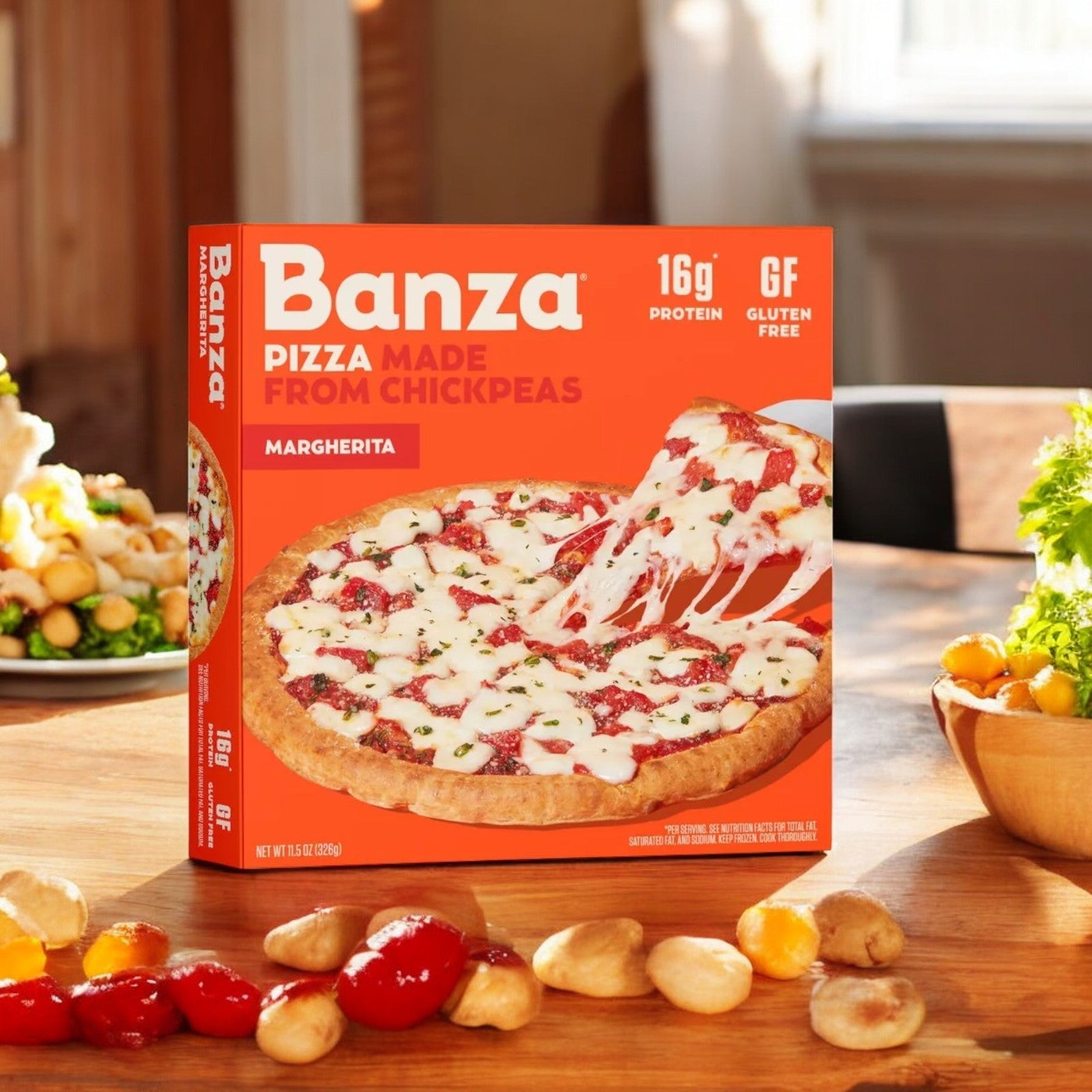 A box of Banza Margherita Pizza-1 Count, from the brand Banza, rests on a wooden table, encircled by fresh vegetables. The packaging highlights its chickpea-based crust and gluten-free composition, featuring 16g of plant-based protein for a deliciously nutritious meal.