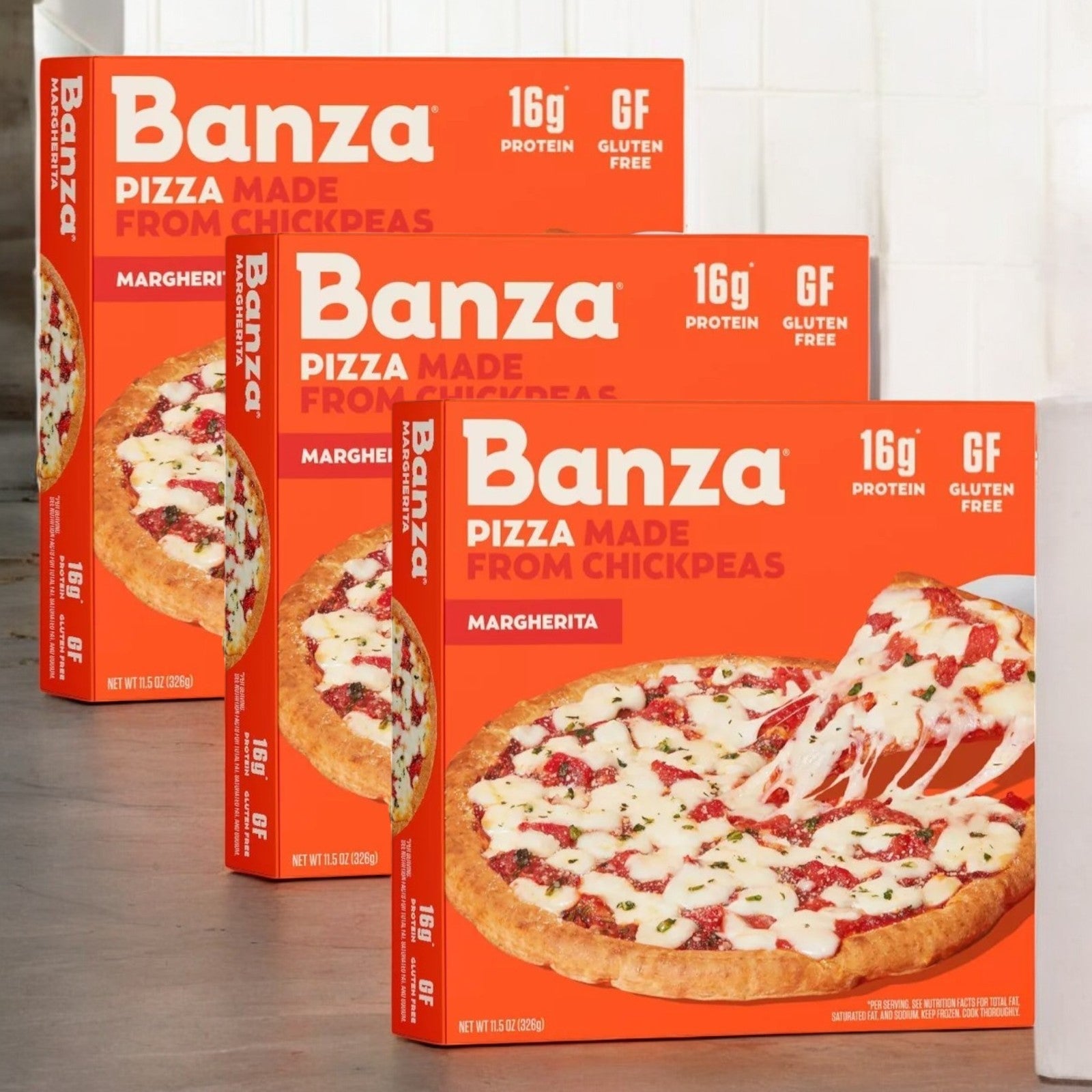 Three Banza Margherita Pizzas with a chickpea crust are on a wooden surface, featuring 16g of plant-based protein and gluten-free labels.